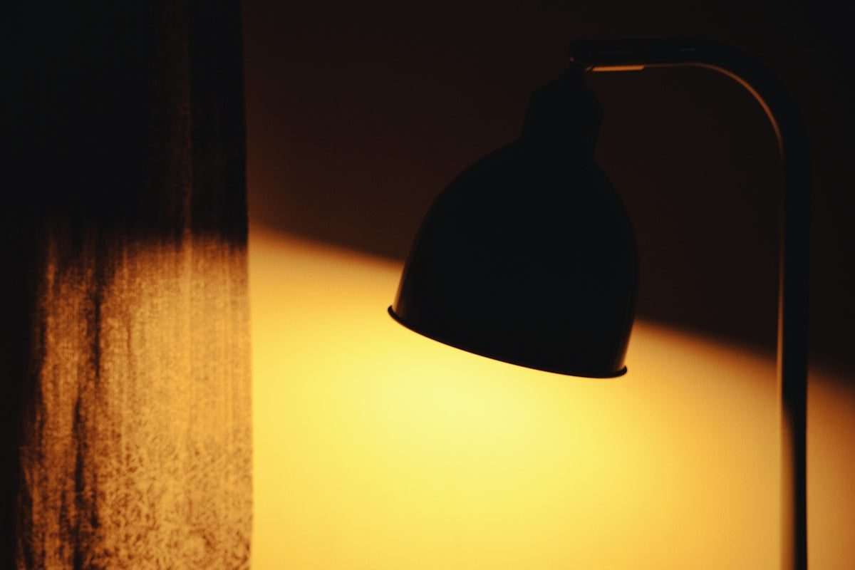 A dark desk lamp casting a warm golden glow on a textured wall
